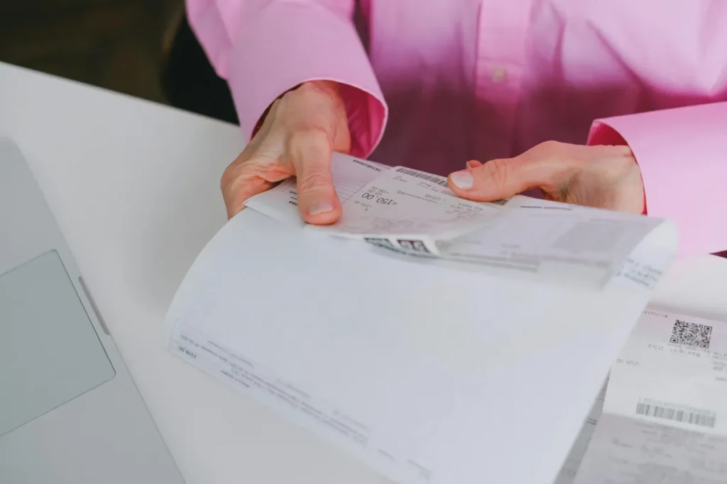 Seseorang mengorganisir nota dan struk pembayaran kertas di atas meja kerja